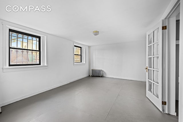 empty room with concrete floors, radiator heating unit, a wealth of natural light, and baseboards