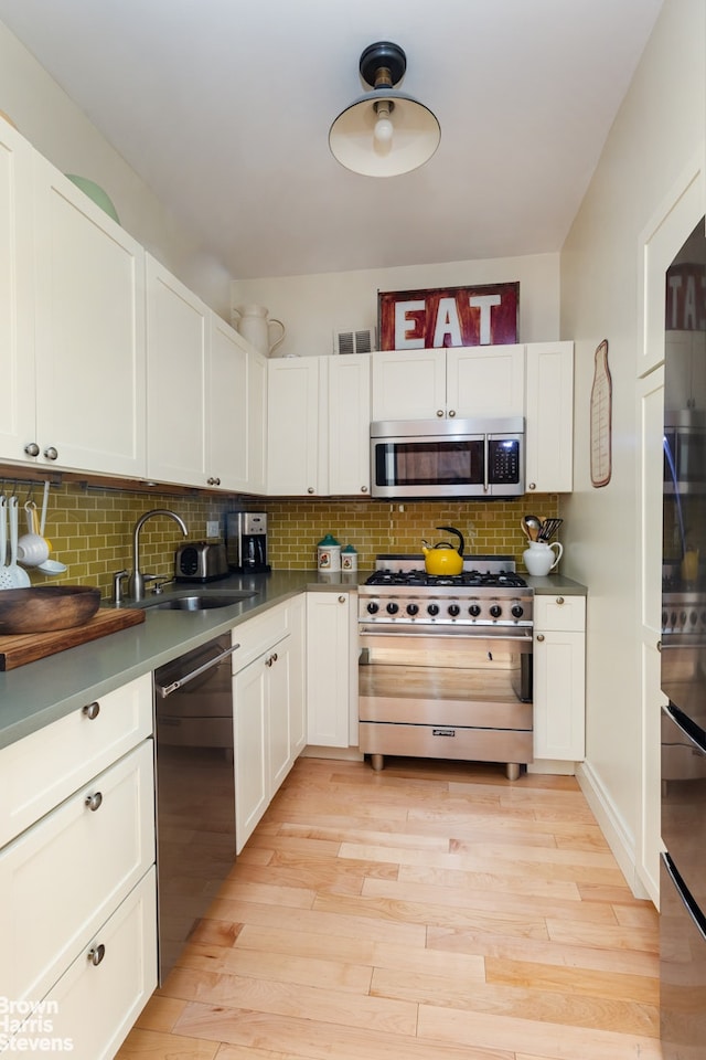 kitchen with stainless steel appliances, decorative backsplash, white cabinetry, and light wood-type flooring