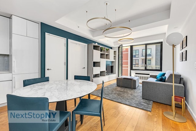 dining area featuring a raised ceiling, light wood-style floors, and baseboards