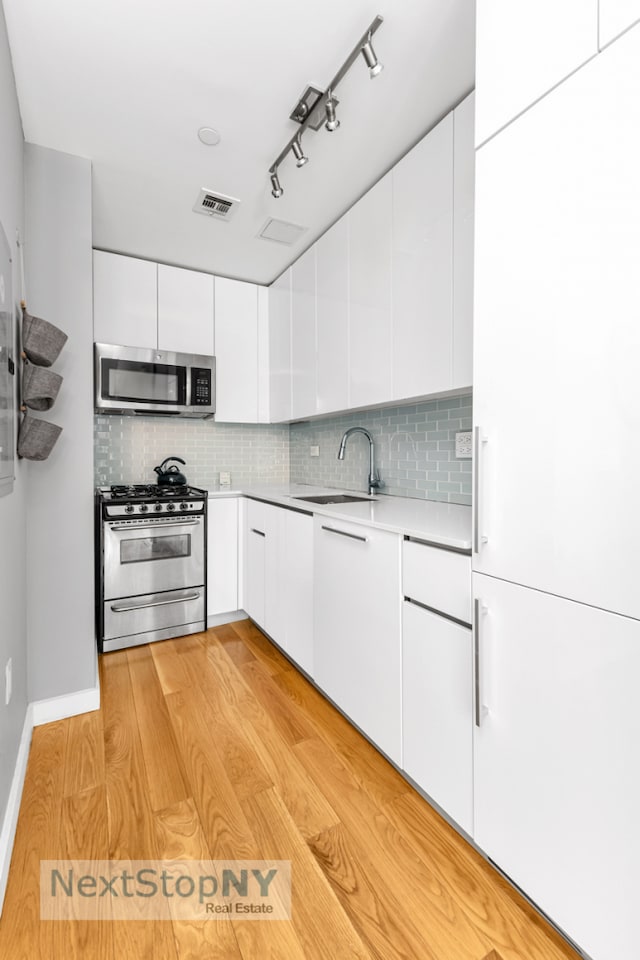 kitchen featuring appliances with stainless steel finishes, a sink, light countertops, and white cabinets
