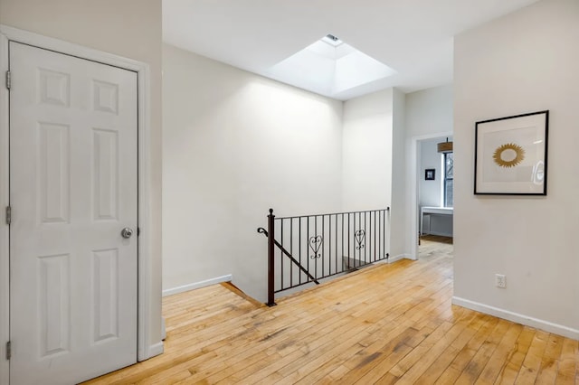 hallway featuring wood-type flooring, a skylight, an upstairs landing, and baseboards
