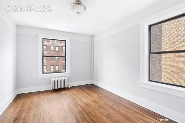 unfurnished room featuring wood finished floors, baseboards, and radiator heating unit