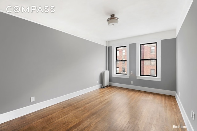 empty room with wood finished floors, baseboards, and radiator heating unit