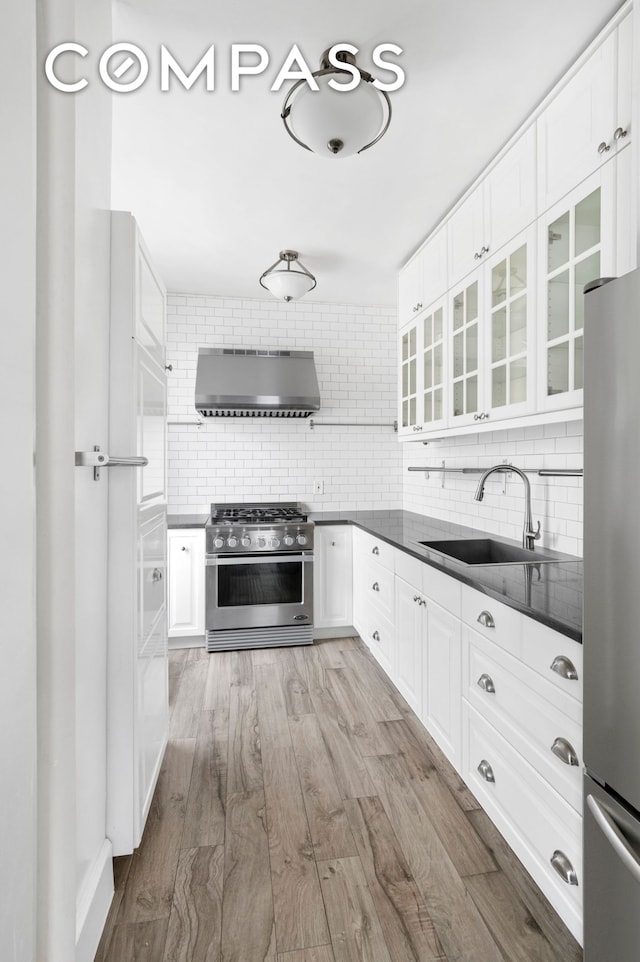 kitchen featuring decorative backsplash, dark countertops, wall chimney range hood, a sink, and stainless steel appliances