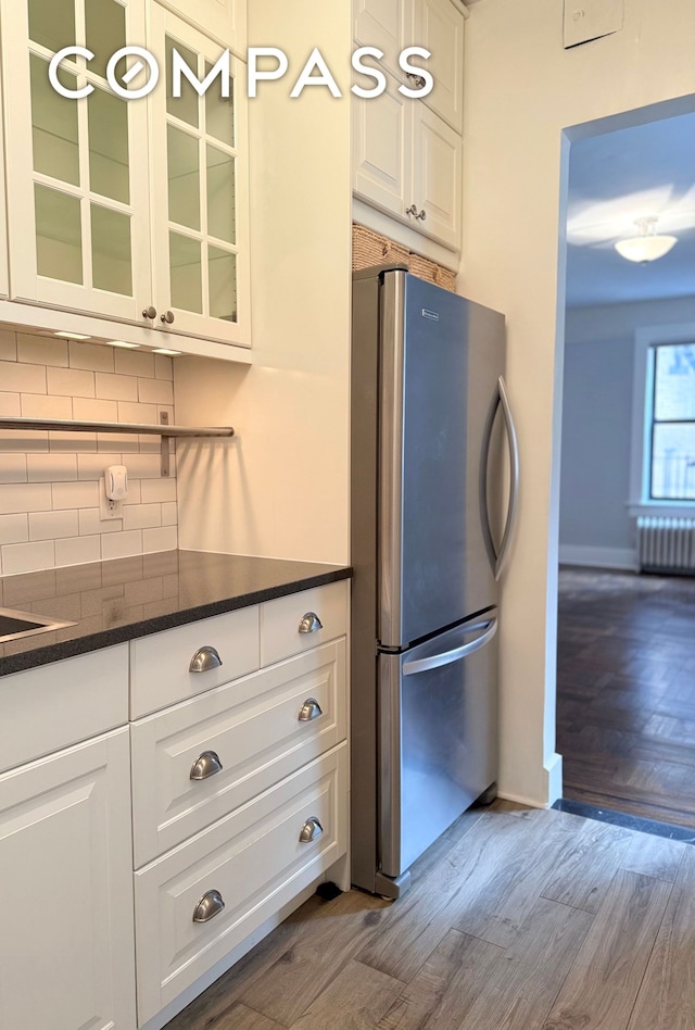 kitchen with radiator, freestanding refrigerator, decorative backsplash, wood finished floors, and glass insert cabinets