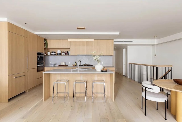 kitchen featuring a sink, a kitchen bar, modern cabinets, open shelves, and light brown cabinets