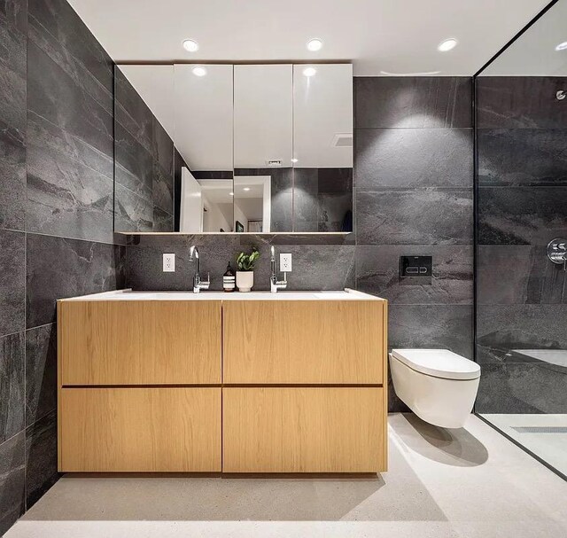 bathroom with a sink, tile walls, double vanity, toilet, and recessed lighting