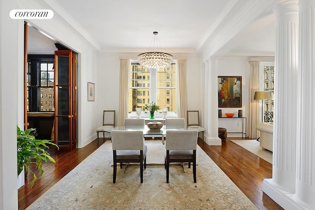 dining room featuring ornate columns, crown molding, a chandelier, and dark wood finished floors