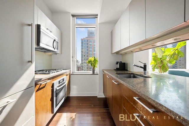 kitchen with a sink, appliances with stainless steel finishes, dark wood-style floors, baseboards, and white cabinetry
