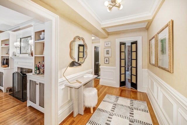 hallway with light wood-type flooring, a notable chandelier, and ornamental molding