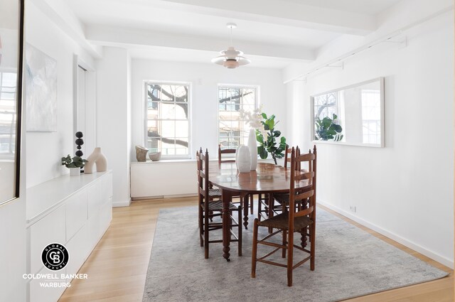 dining space with light wood-style flooring, beam ceiling, and baseboards