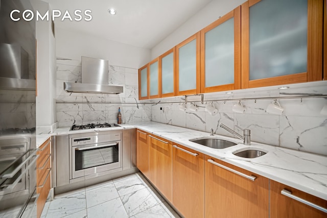 kitchen with appliances with stainless steel finishes, a sink, wall chimney exhaust hood, and light stone counters