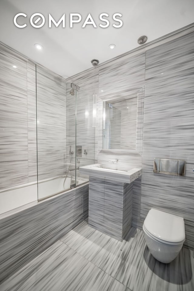 full bathroom with tile walls, vanity, tile patterned flooring, toilet, and bath / shower combo with glass door
