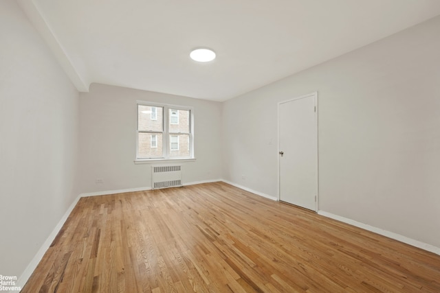 empty room featuring light wood finished floors, radiator heating unit, and baseboards
