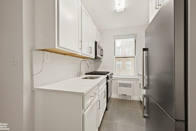 kitchen with radiator, a sink, tile patterned floors, white cabinets, and appliances with stainless steel finishes