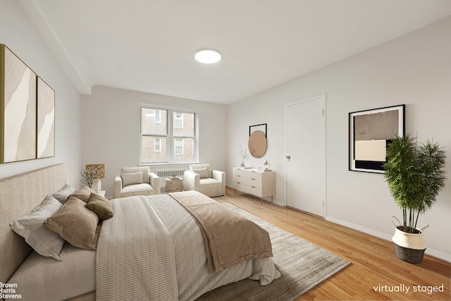 bedroom with baseboards, radiator, and light wood-style flooring