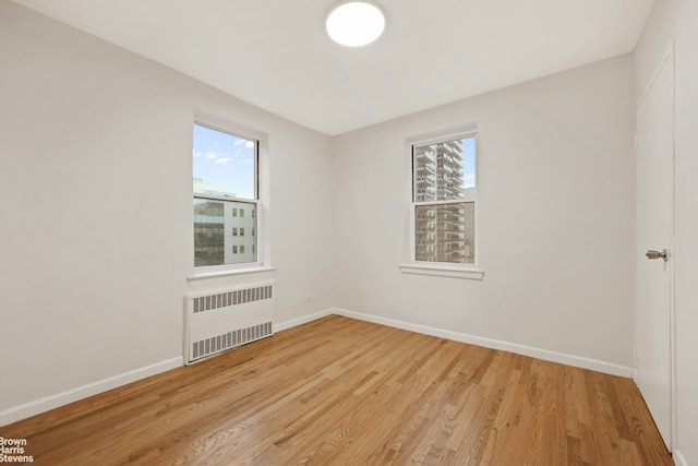 spare room with baseboards, light wood finished floors, and radiator