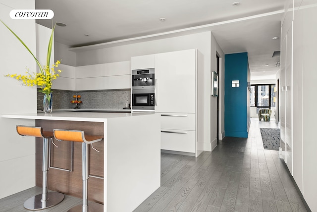 40 Broad St Unit Ph2Ce, New York City, NY 10004 - kitchen with modern cabinets, wood finished floors, white cabinets, tasteful backsplash, and a breakfast bar