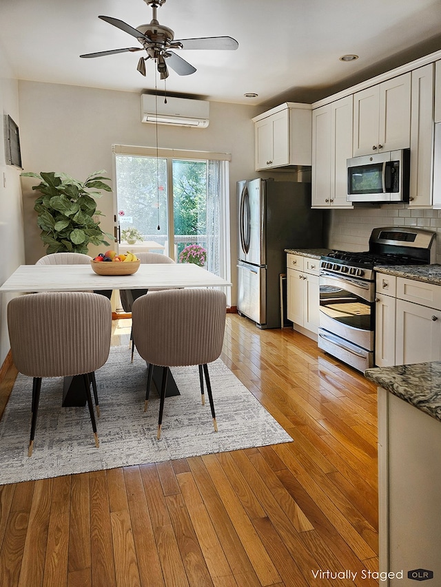 230 26th St, New York City, NY 11232 - kitchen featuring appliances with stainless steel finishes, a wall mounted air conditioner, a ceiling fan, light wood-type flooring, and white cabinets