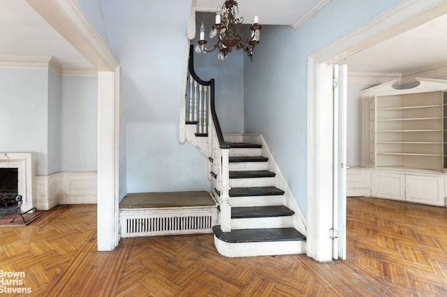 staircase featuring ornamental molding, an inviting chandelier, a brick fireplace, and visible vents