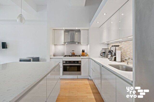 15 Broad St Unit 2714, New York City, NY 10005 - kitchen featuring appliances with stainless steel finishes, modern cabinets, wall chimney range hood, a sink, and white cabinets