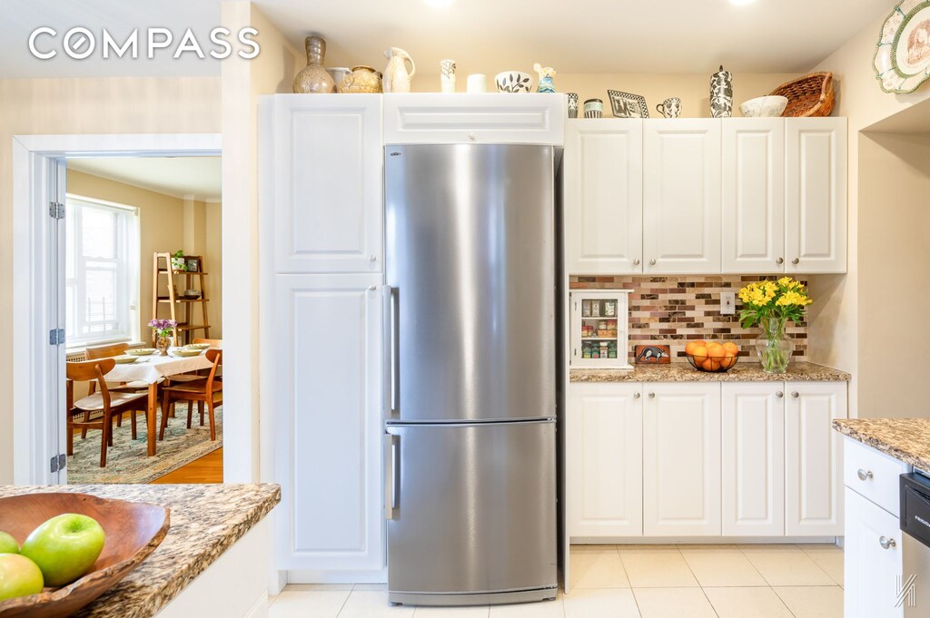 34-41 85th St Unit 4P, New York City, NY 11372 - kitchen with freestanding refrigerator, white cabinetry, backsplash, light stone counters, and light tile patterned flooring