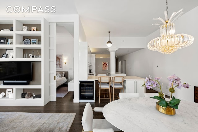 dining space with wine cooler, decorative columns, wood finished floors, and a chandelier