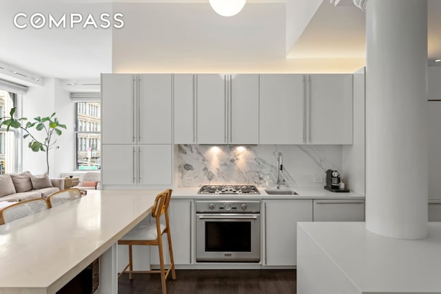 kitchen featuring stainless steel appliances, a sink, tasteful backsplash, light countertops, and dark wood-style floors