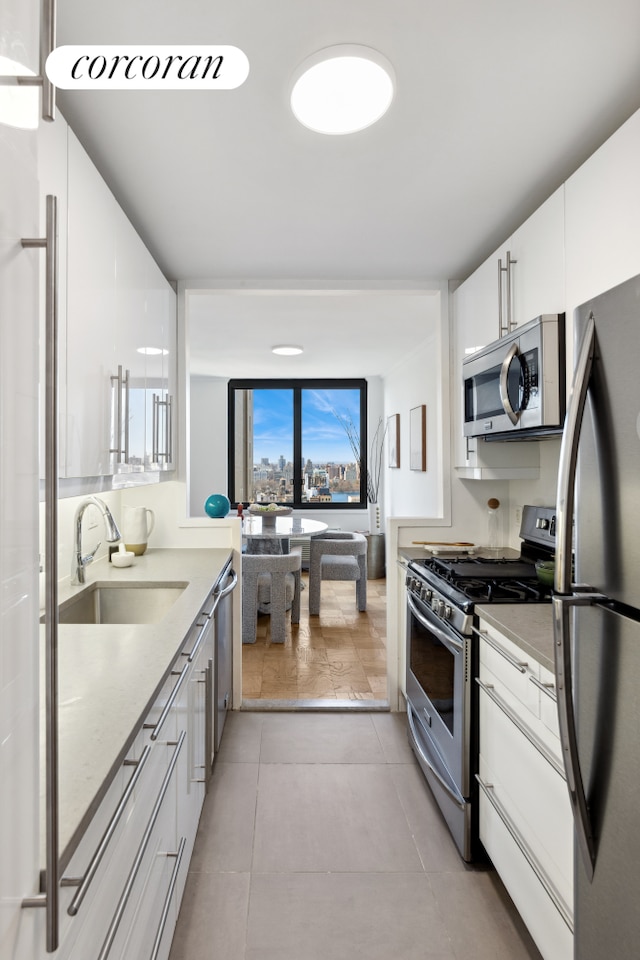 kitchen with appliances with stainless steel finishes, a sink, white cabinetry, light tile patterned floors, and light stone countertops