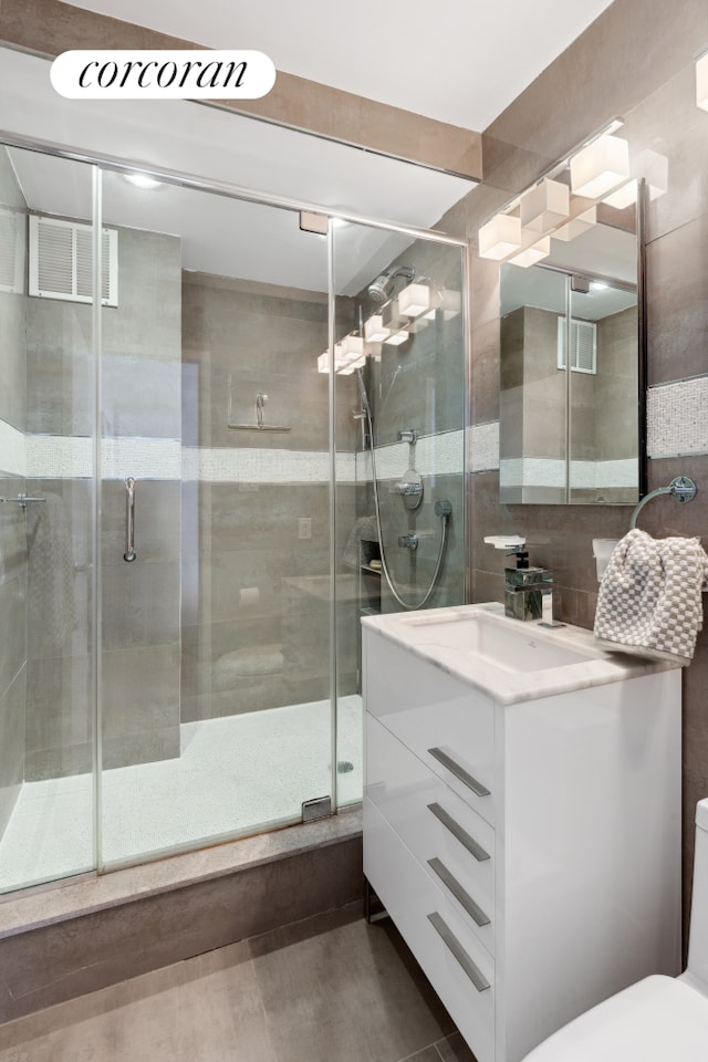 bathroom with a shower stall, vanity, tile walls, and toilet