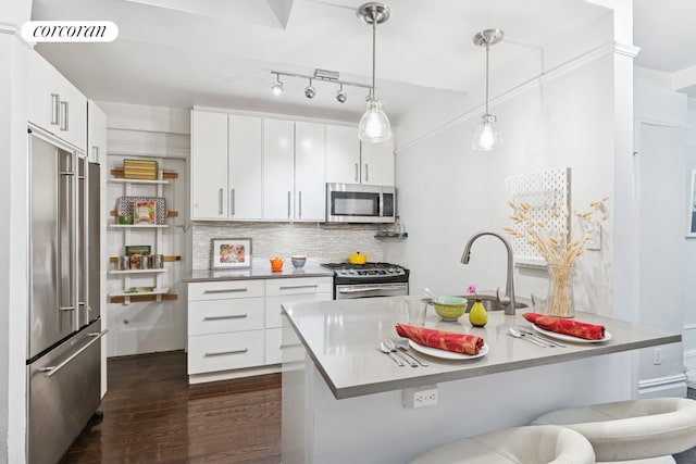 kitchen with appliances with stainless steel finishes, dark wood-type flooring, tasteful backsplash, white cabinetry, and pendant lighting