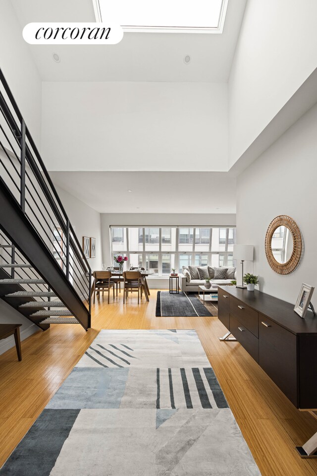 living area with a towering ceiling, stairway, light wood-style flooring, and plenty of natural light