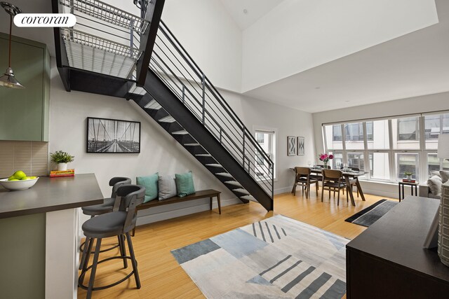 living area featuring light wood-style floors, a high ceiling, baseboards, and stairs
