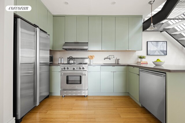 kitchen with green cabinetry, decorative backsplash, a sink, appliances with stainless steel finishes, and under cabinet range hood