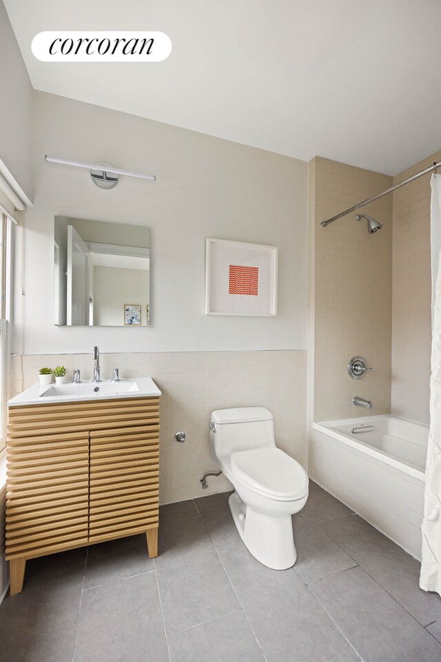 bathroom featuring shower / bathtub combination with curtain, vanity, tile patterned floors, toilet, and a wainscoted wall