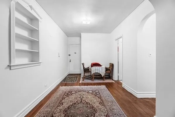 hallway featuring arched walkways, wood finished floors, and baseboards