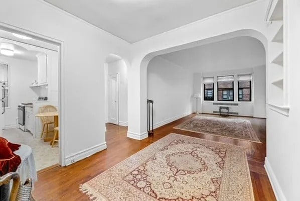corridor with arched walkways, baseboards, and wood finished floors