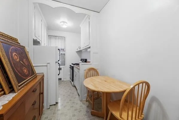 kitchen with gas range oven, white fridge, white cabinets, and light floors