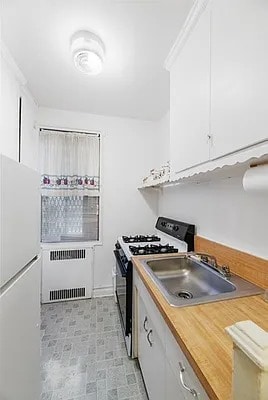 kitchen featuring gas stove, white cabinetry, freestanding refrigerator, radiator, and a sink