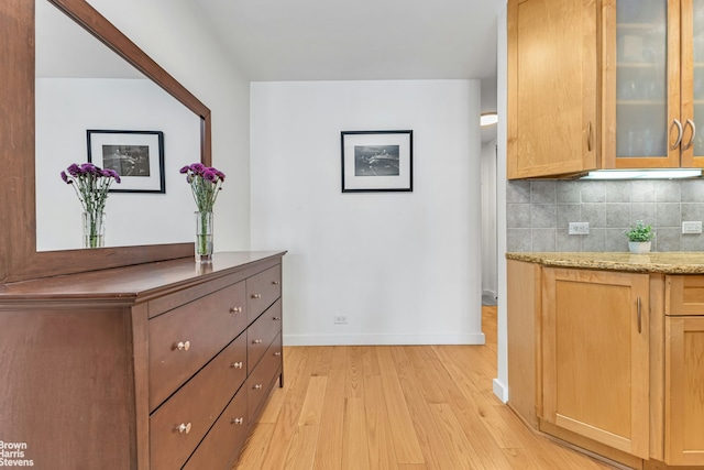 155 E 38th St Unit 16B, New York City, NY 10016 - kitchen with light wood-type flooring, decorative backsplash, baseboards, glass insert cabinets, and light stone counters