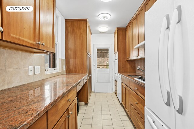 43 Charlton St, New York City, NY 10014 - kitchen with brown cabinets, dark stone countertops, light tile patterned flooring, freestanding refrigerator, and tasteful backsplash