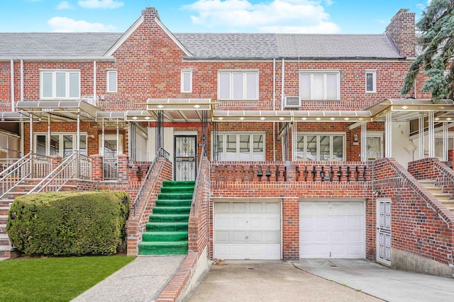 multi unit property featuring a garage, brick siding, concrete driveway, and stairs