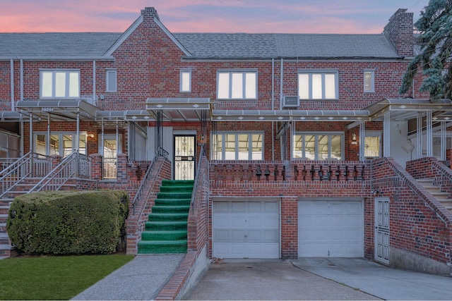 townhome / multi-family property with an attached garage, brick siding, driveway, and stairway