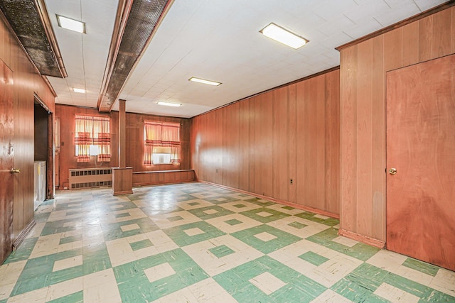 empty room with light floors, wooden walls, and radiator heating unit