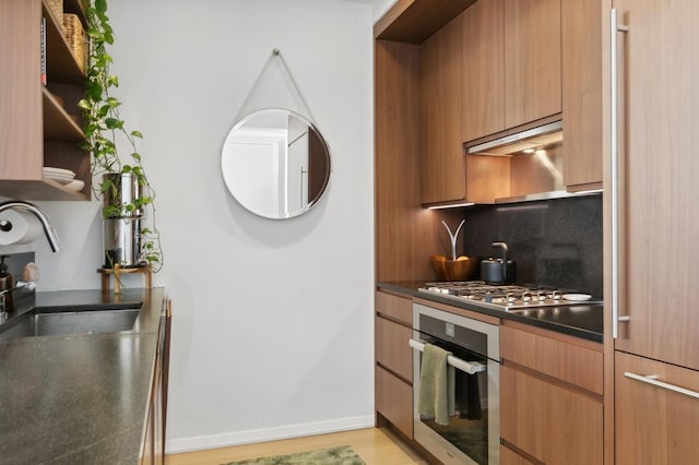 kitchen featuring dark countertops, modern cabinets, decorative backsplash, open shelves, and appliances with stainless steel finishes