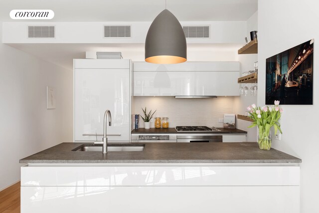 kitchen featuring a sink, open shelves, stainless steel gas stovetop, backsplash, and white cabinets
