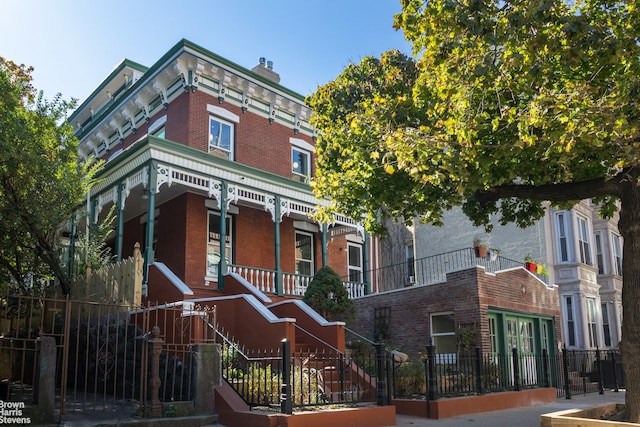 italianate home featuring stairway, a chimney, a fenced front yard, a porch, and brick siding