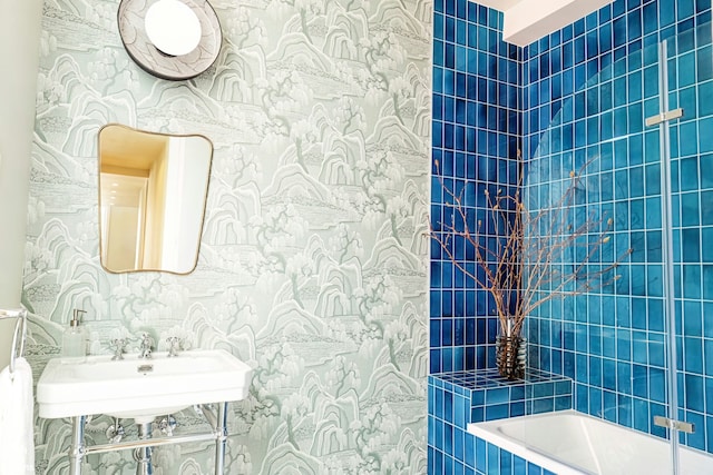 bathroom with washtub / shower combination, wallpapered walls, and a sink