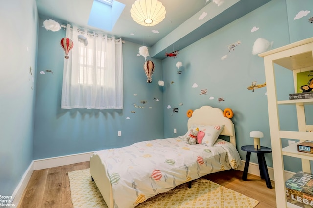bedroom featuring a skylight, baseboards, and wood finished floors