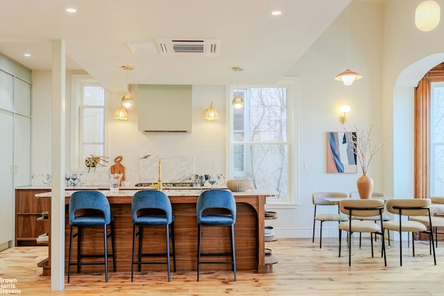 kitchen featuring arched walkways, light wood-type flooring, visible vents, and a kitchen breakfast bar